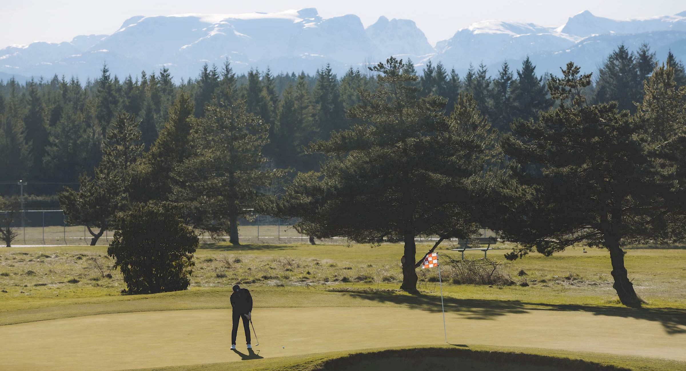 A person putting on a green with mountains in the background
