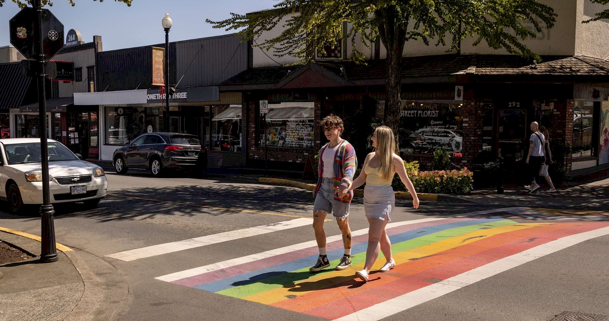 Two people walking across a rainbow crosswalk in Downtown Courtenay